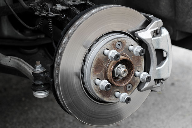 A close-up of fresh brake discs and high-performance caliper behind a clean alloy wheel in the garage