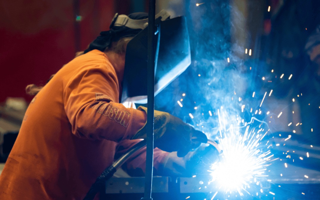 A skilled fabricator welding a vehicle chassis with bright glowing sparks in the garage